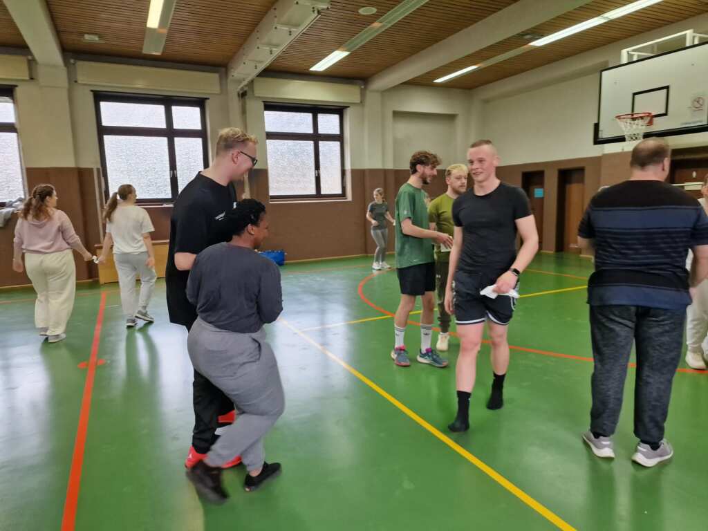 Gruppe von Menschen in einer Turnhalle, einzelne Personen zu erkennen.